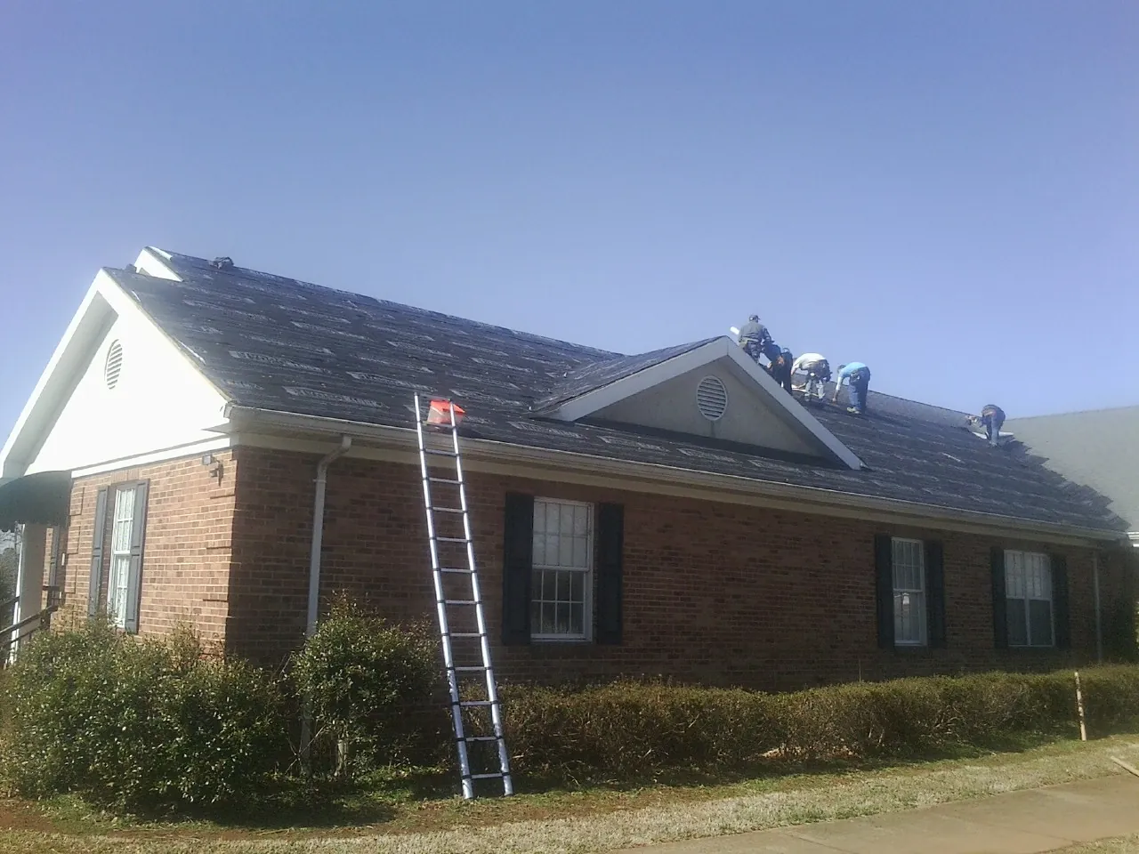 Crew tearing shingles off a brick ranch roof with a ladder set — Emergency Roof Repair work by our crew in Etowah