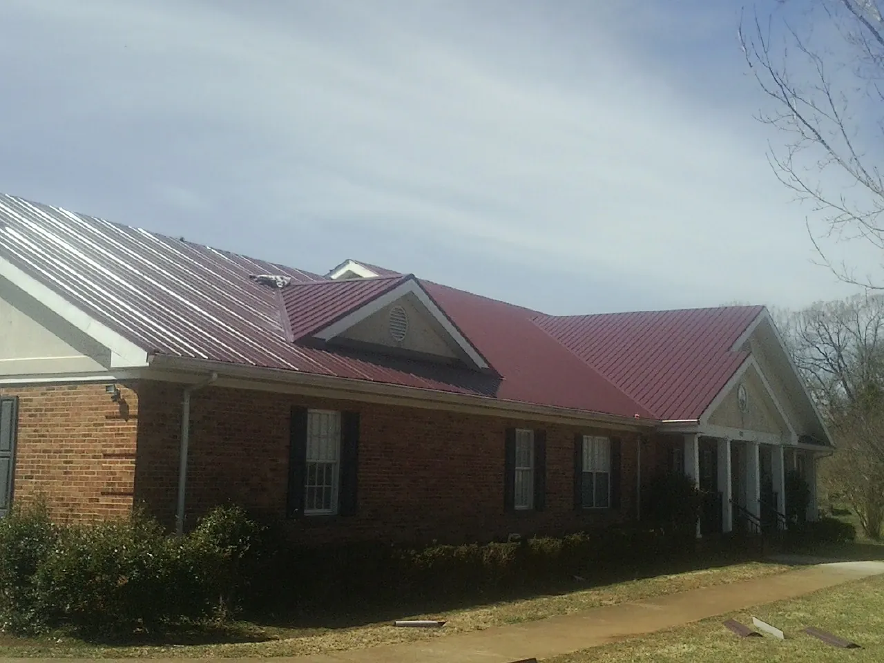 Red metal roof with gabled entries on a long brick building, from a Hail Damage Roof Repair job in Etowah