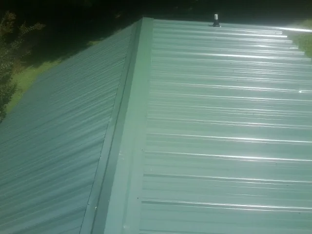 New green metal panels meeting at the ridge of a roof — Flat Roof Repair work by our crew in Etowah