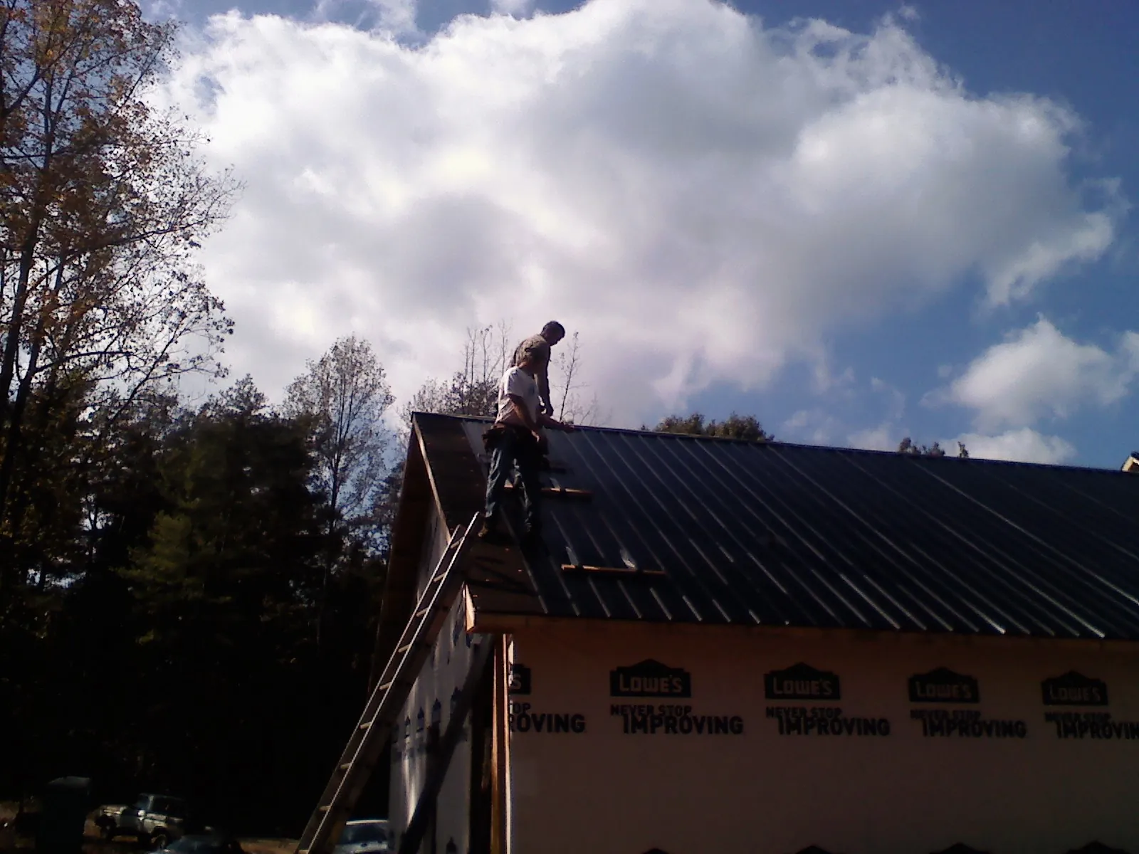 Roofer fastening dark metal panels high against a cloudy sky, from a Roof Inspection job in Etowah